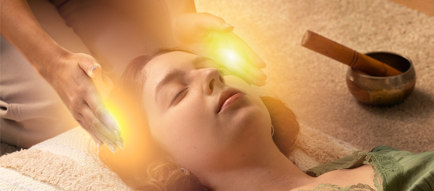 Soin énergétique par imposition des mains sur le troisième œil d'une femme allongée, luminosité dorée et bol tibétain
