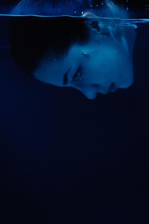 Femme nageant sous l’eau, visage en plongée silencieuse, ambiance bleutée et sereine évoquant l’équilibre intérieur à retrouver.