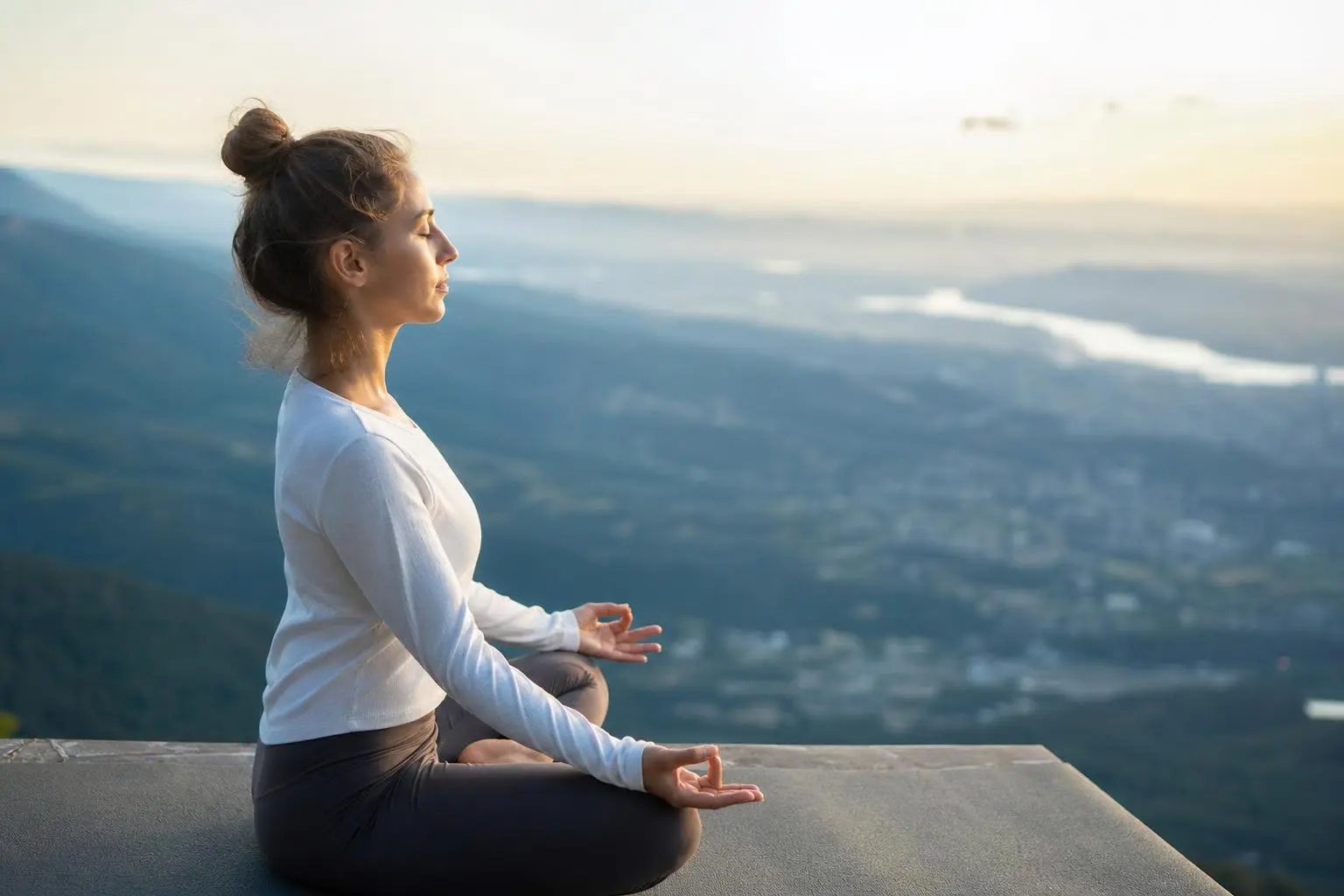 Femme assise en position de méditation sur un balcon, panorama montagnard au lever du soleil, exprimant calme et équilibre émotionnel. comment retrouver son équilibre émotionnel