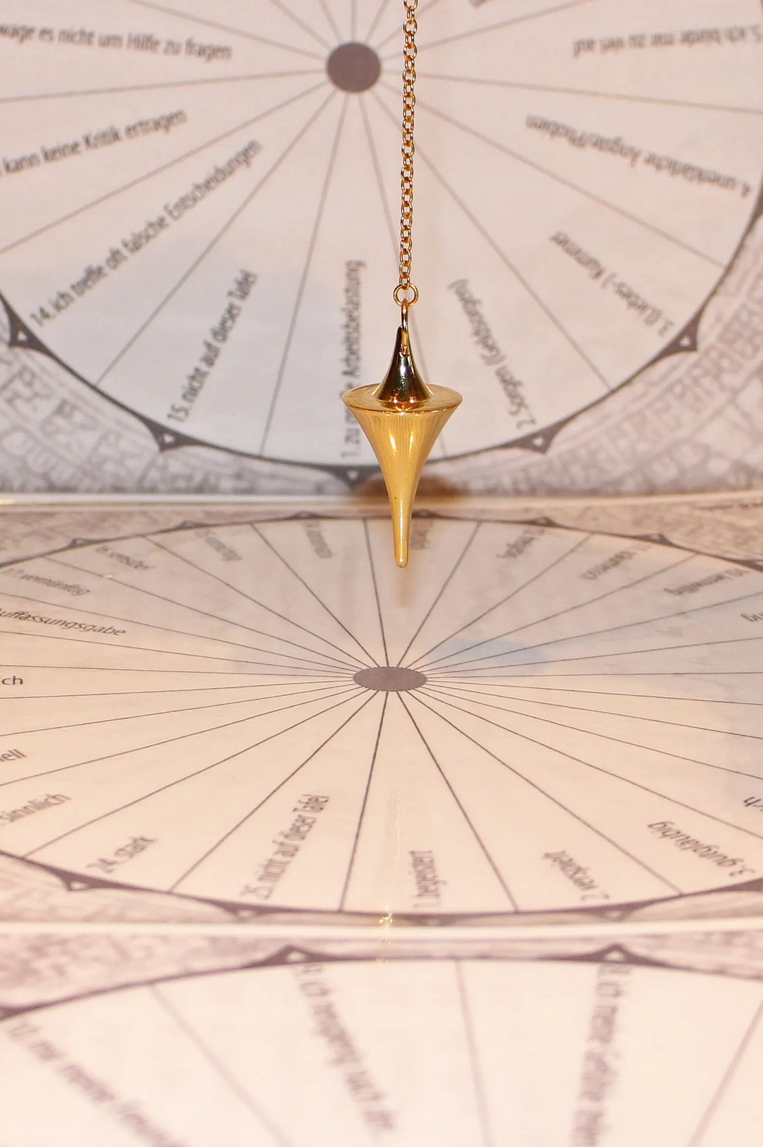 Pendentif doré en forme de cône suspendu au-dessus d'un disque astrologique, motifs circulaires et textes gravés en arrière-plan.