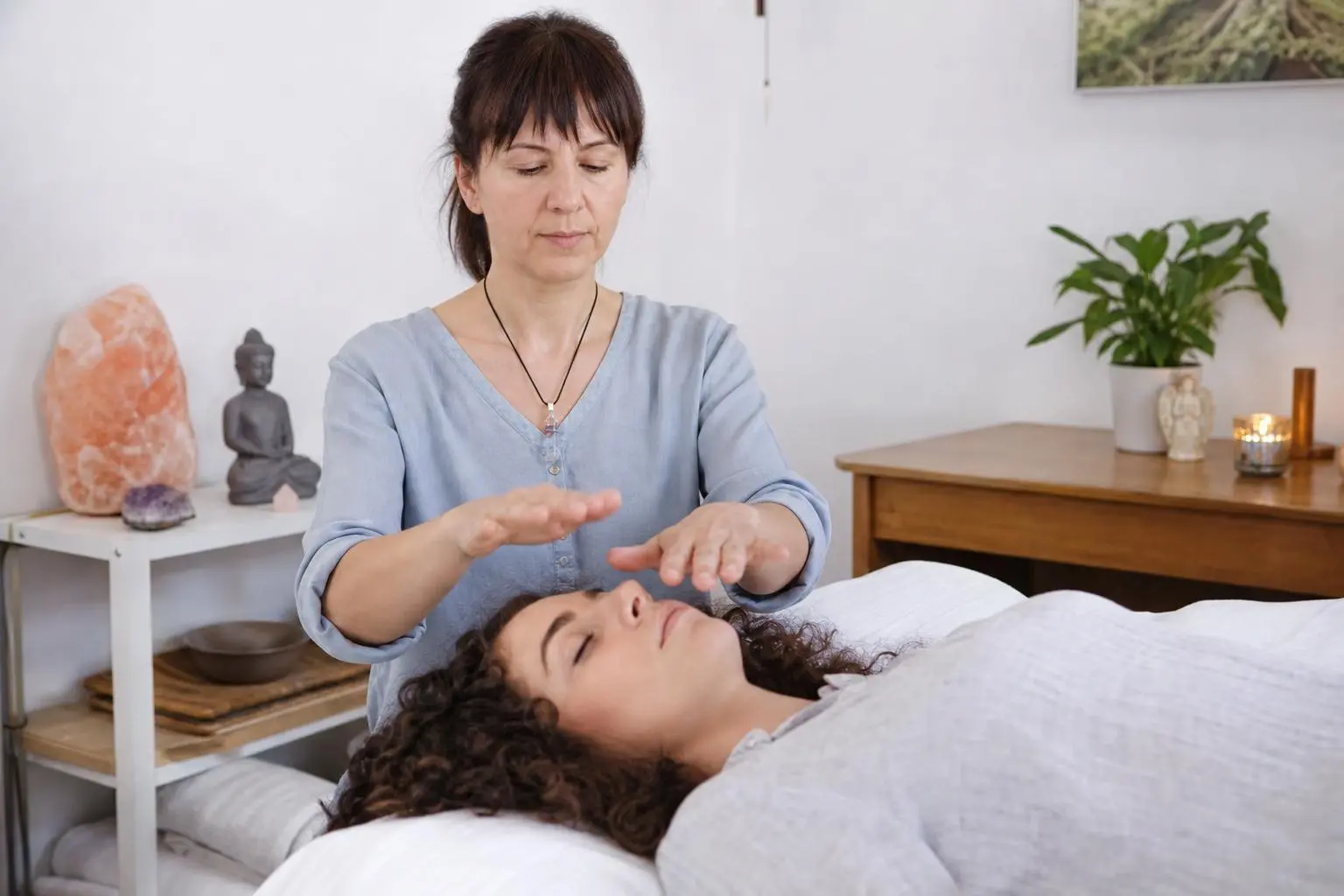 Praticienne posant les mains au-dessus d'une personne allongée, séance de soin ou thérapie pour commenter retrouver son équilibre émotionnel.