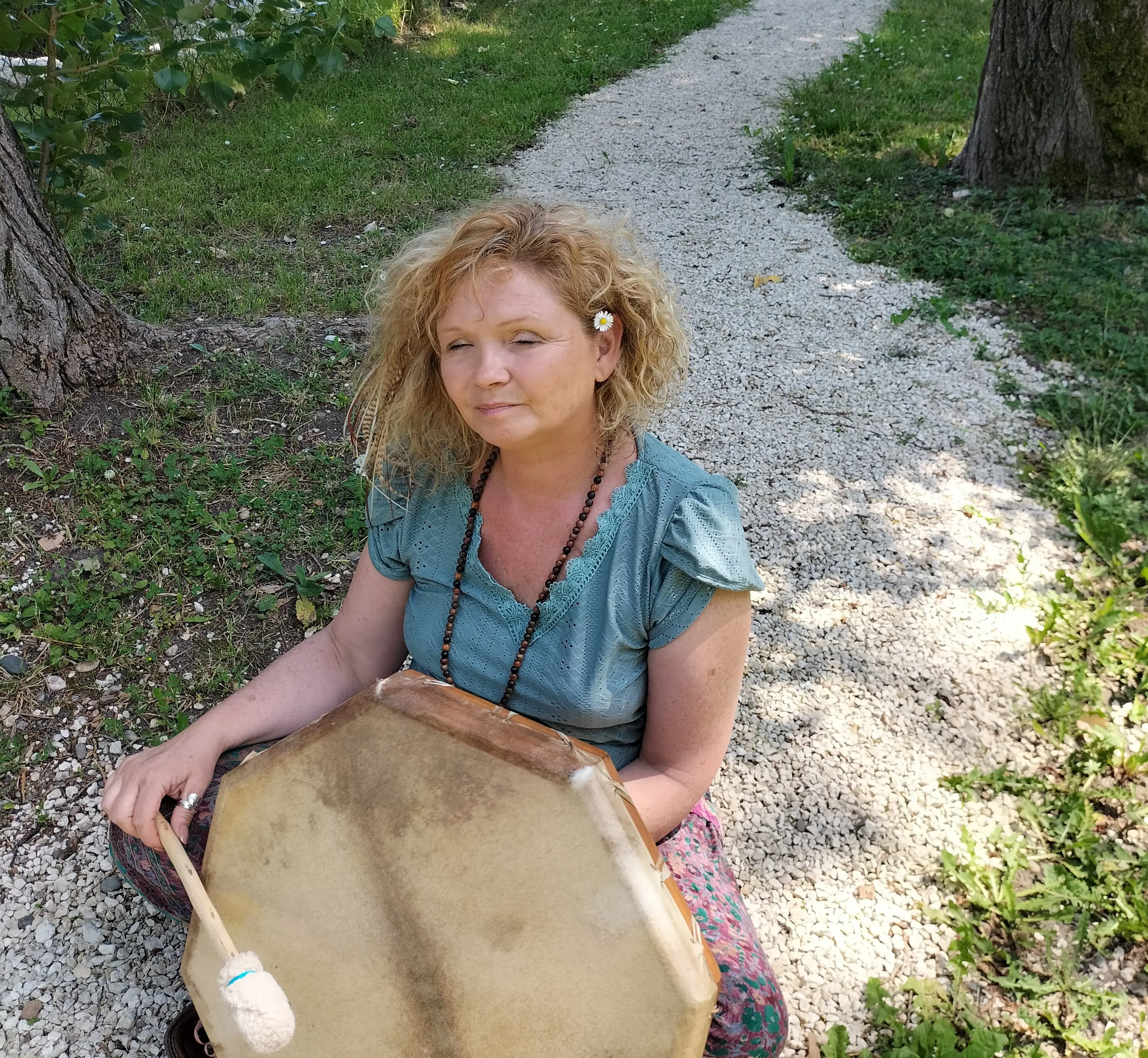 Sophie Latour assise en plein air sur un chemin de gravier, tenant un grand tambour zen et une baguette de percussion.