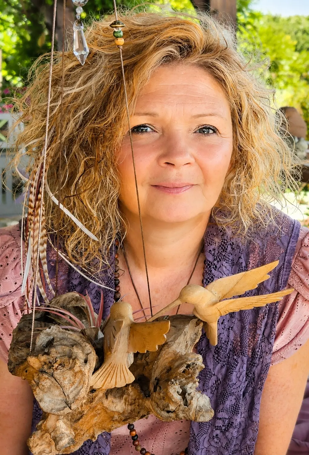 Sophie Latour, médium et thérapeute énergéticienne, à l’air calme avec des cheveux bouclés, porte une sculpture suspendue en bois et plumes autour du cou, en extérieur.