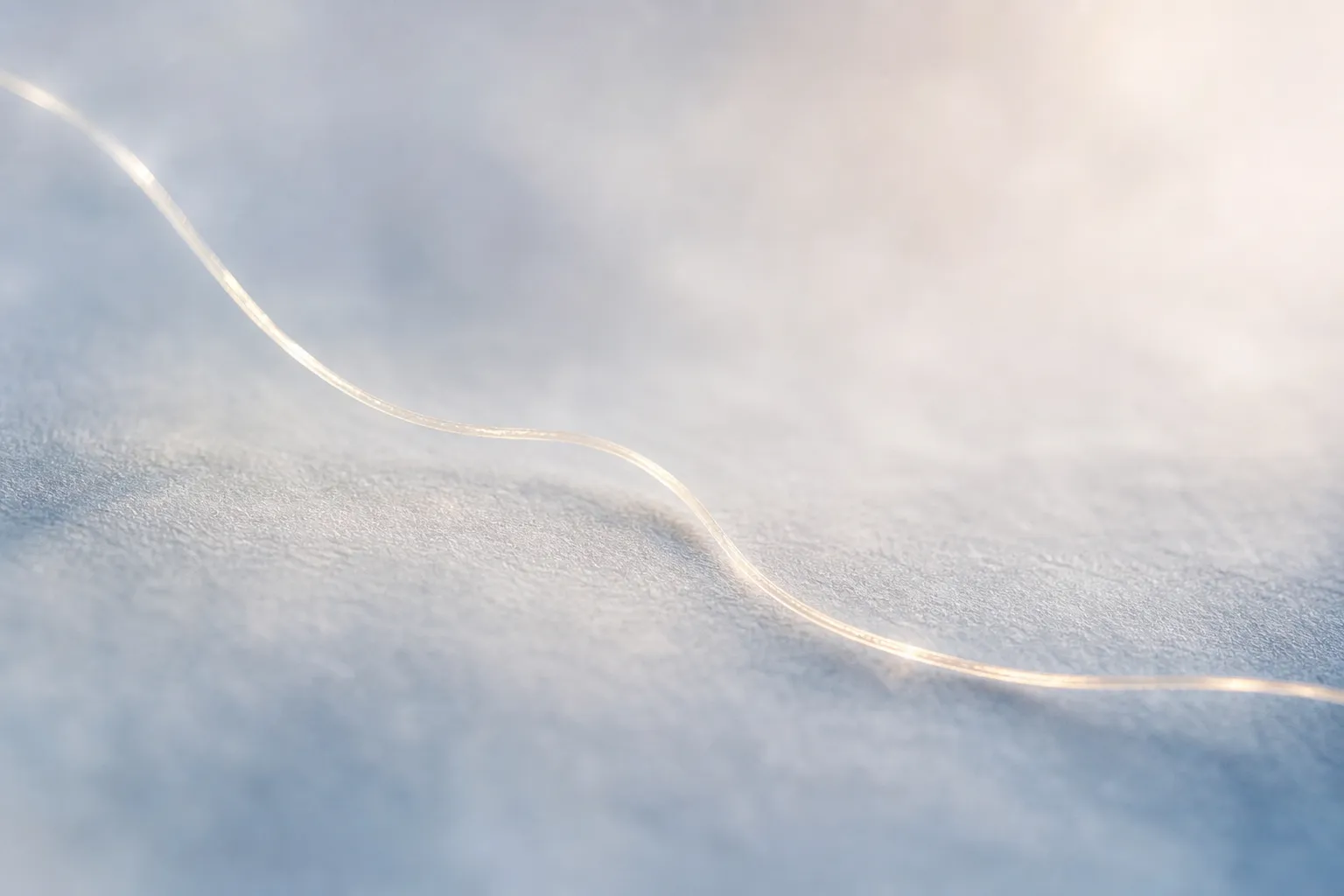 Fil tendu sur une surface blanche et douce, évoquant une ligne légère et ondulée symbolisant l’hypersensibilité et douleur physique.