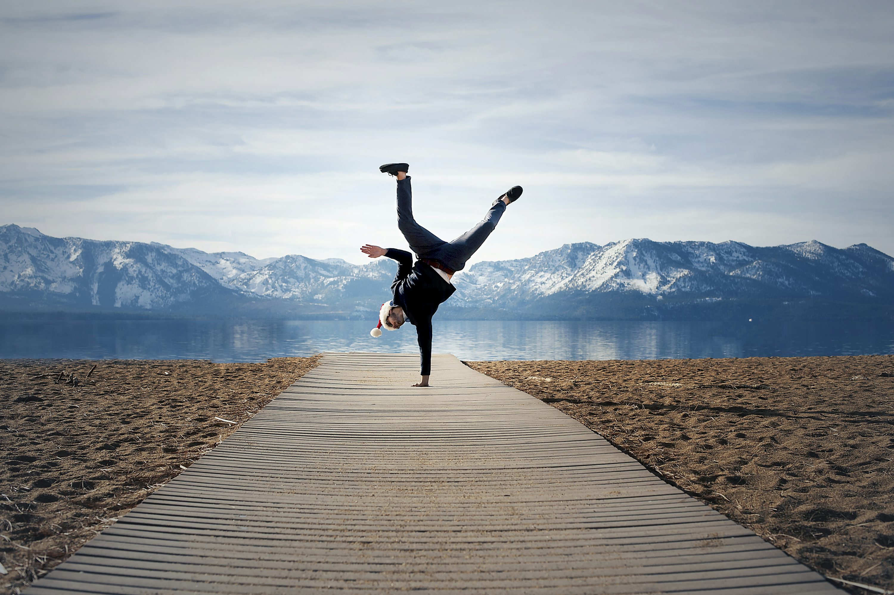 Une personne soutenue sur une main sur un chemin en bois, les jambes en l’air dans une pose d’équilibre sur une plage devant