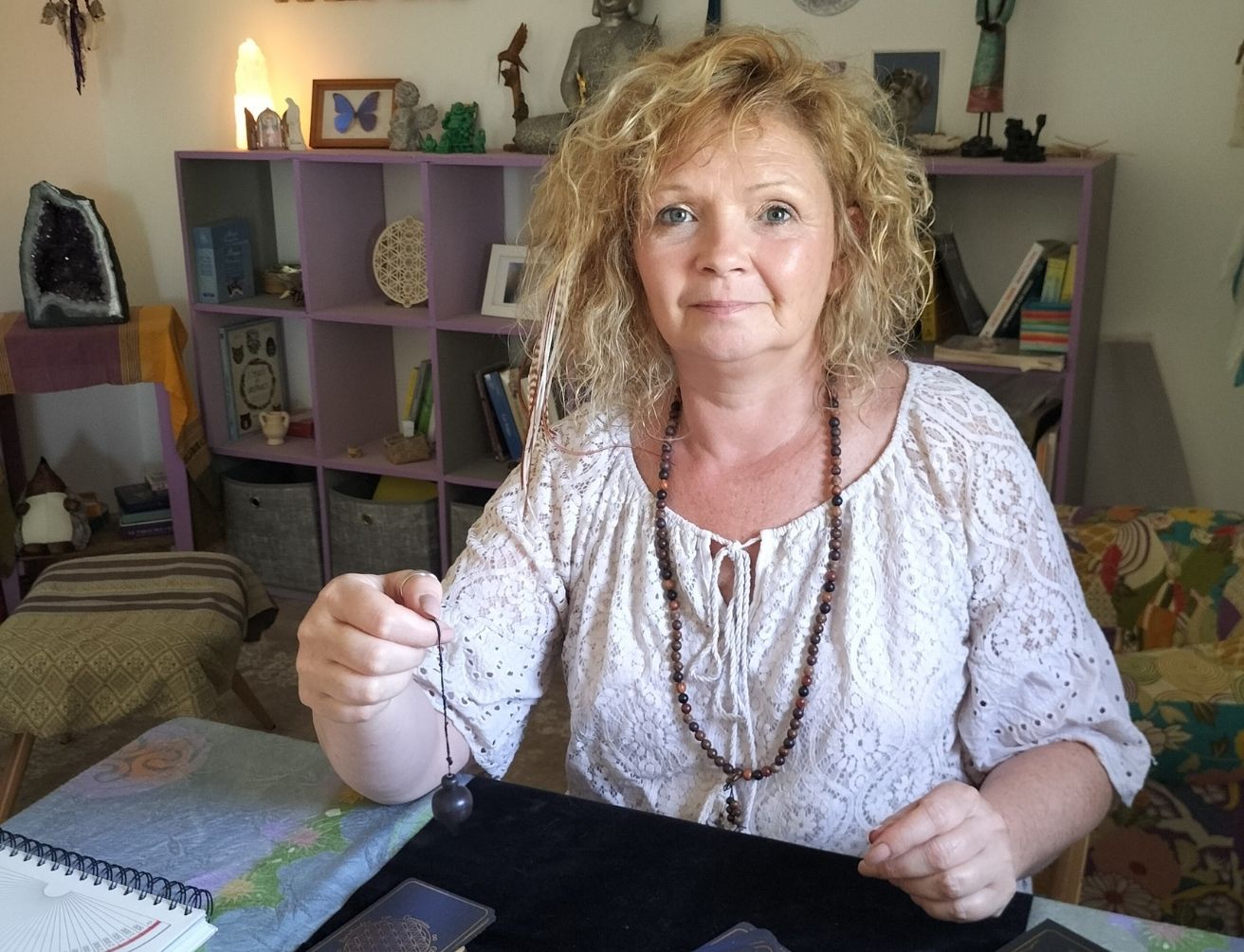 Une femme assise à une table tient une boule pendante reliée à une corde, dans un espace intérieur avec des étagères et des