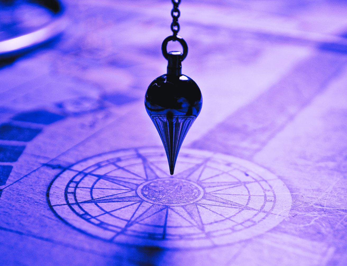 Pendentif noir en forme de pointe suspendu au-dessus d’un diagramme circulaire gravé sur fond violet.