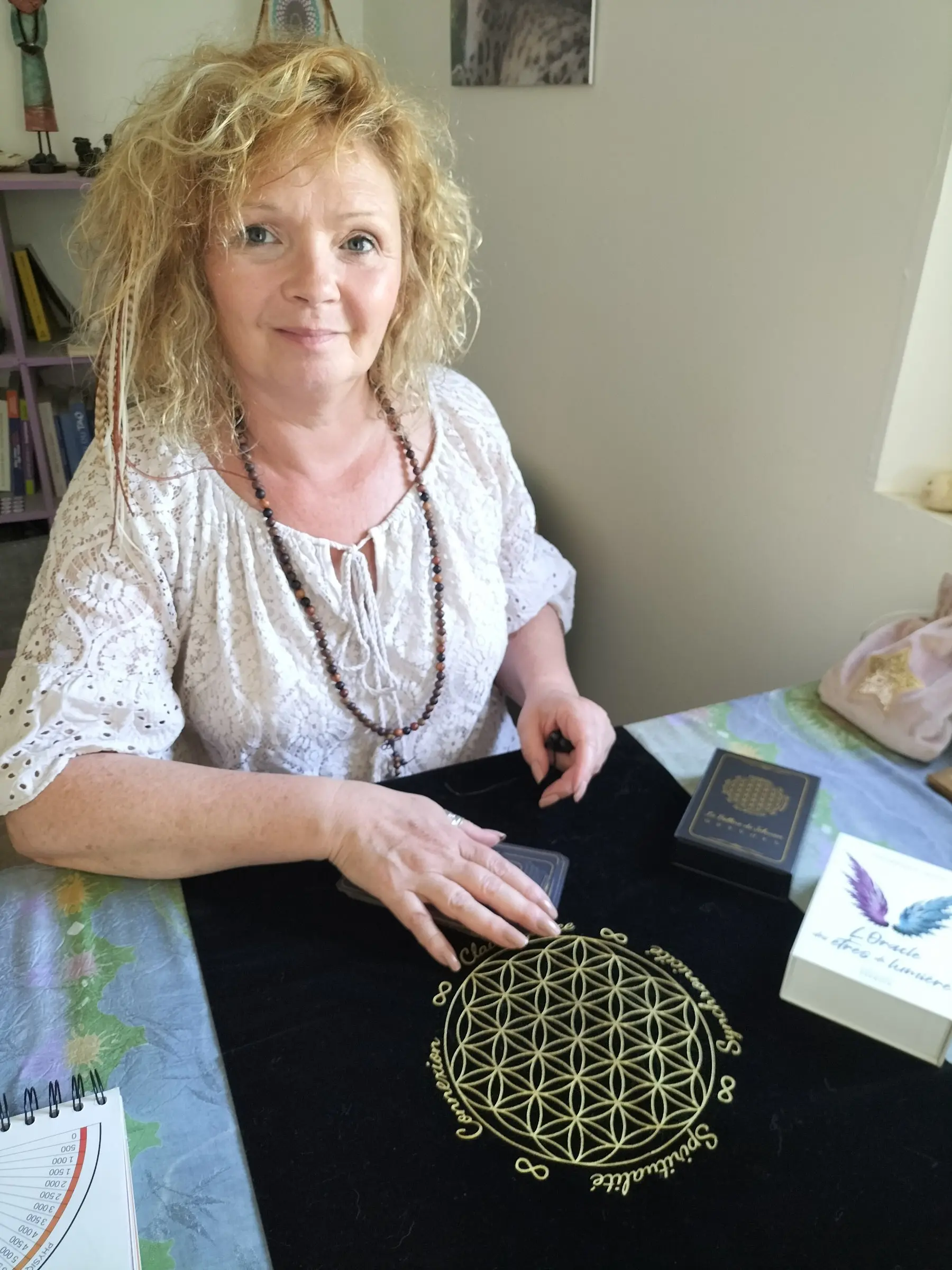 Sophie Latour lors d’une séance, assise à une table avec tapis d’occultation géométrique doré, cartes et boîte, ambiance