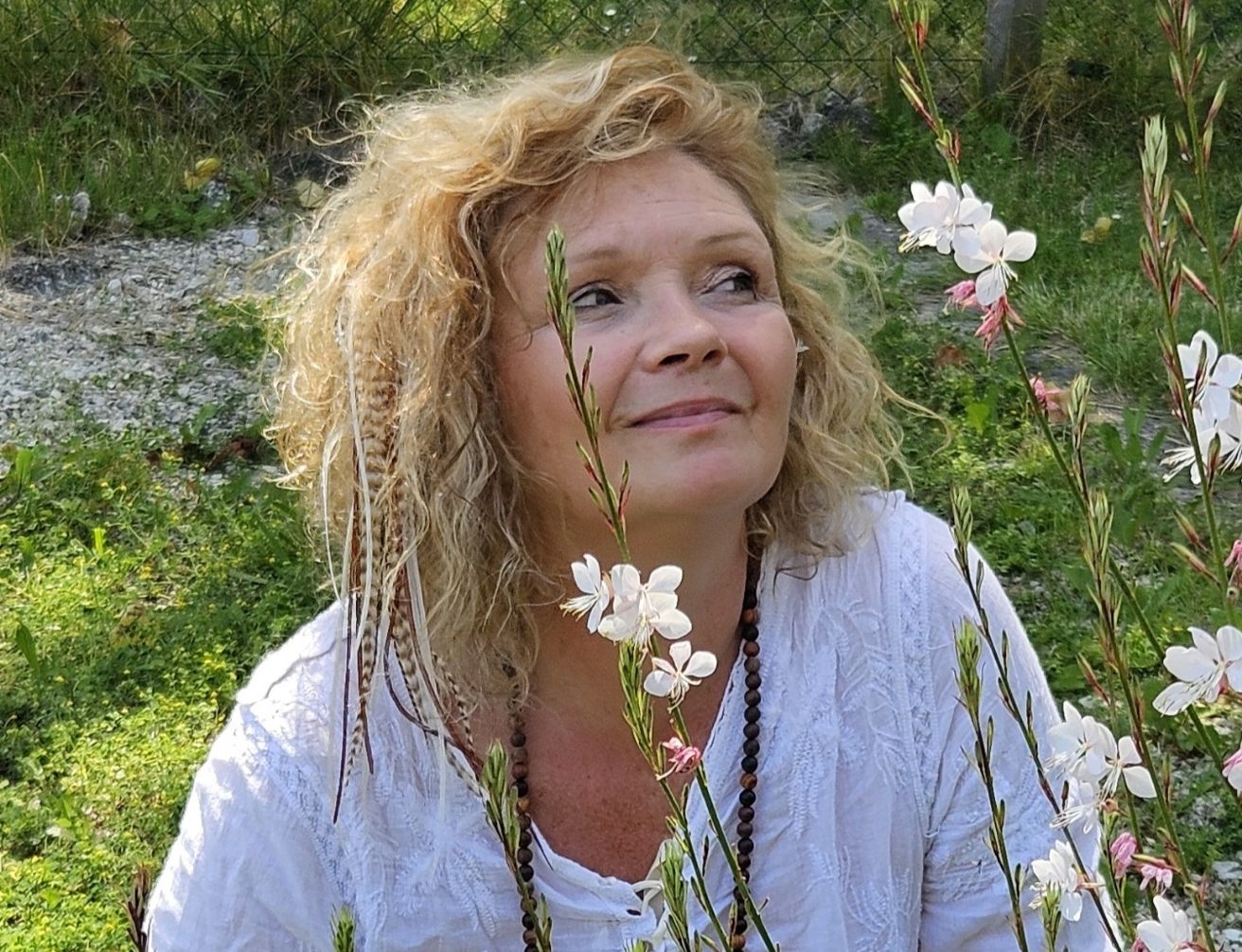 Sophie Latour, médium et thérapeute énergéticienne, assise en extérieur parmi des fleurs blanches et des herbes, regard